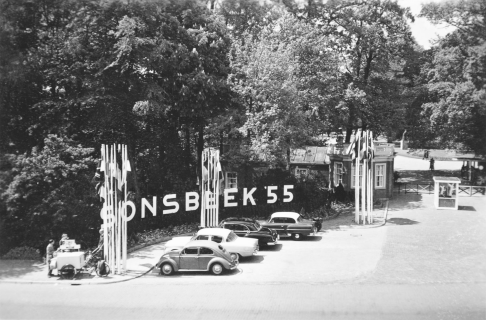 Op deze zwart-wit foto zijn vier geparkeerde auto’s te zien, langs de Apeldoornseweg, bij de ingang van Park Sonsbeek. In het plantsoen langs de stoep die naar de ingang leidt, staan grote witte letters die het woord ‘Sonsbeek’ vormen, gevolgd door vijfenvijftig. Verder staan er op drie plekken op de stoep vlaggenmasten met Europese vlaggen, het zijn drie plekken ieder circa 8 vlaggenmasten.